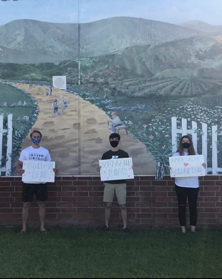 Titan Ambassadors Trent Norton, Evan Asakawa, and Amelia Zolzer social distance and take a photo in front of the Garden Road Elementary School mural with their welcome back posters and Poway apparel.