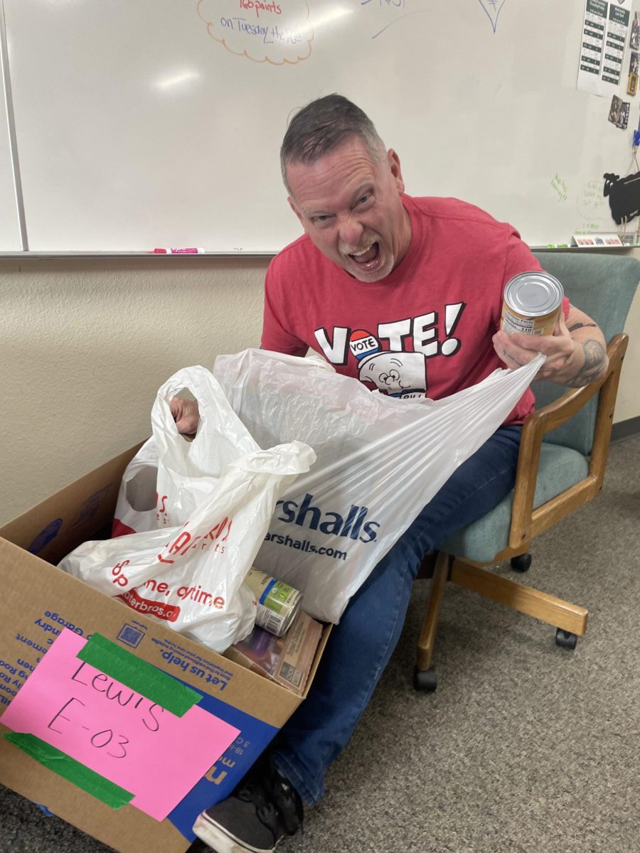 Curt Lewis is showing off the cans that his AP U.S. History and AP World History students have brought in for the food drive. He has challenged other teachers to try to match his classes collection. 			