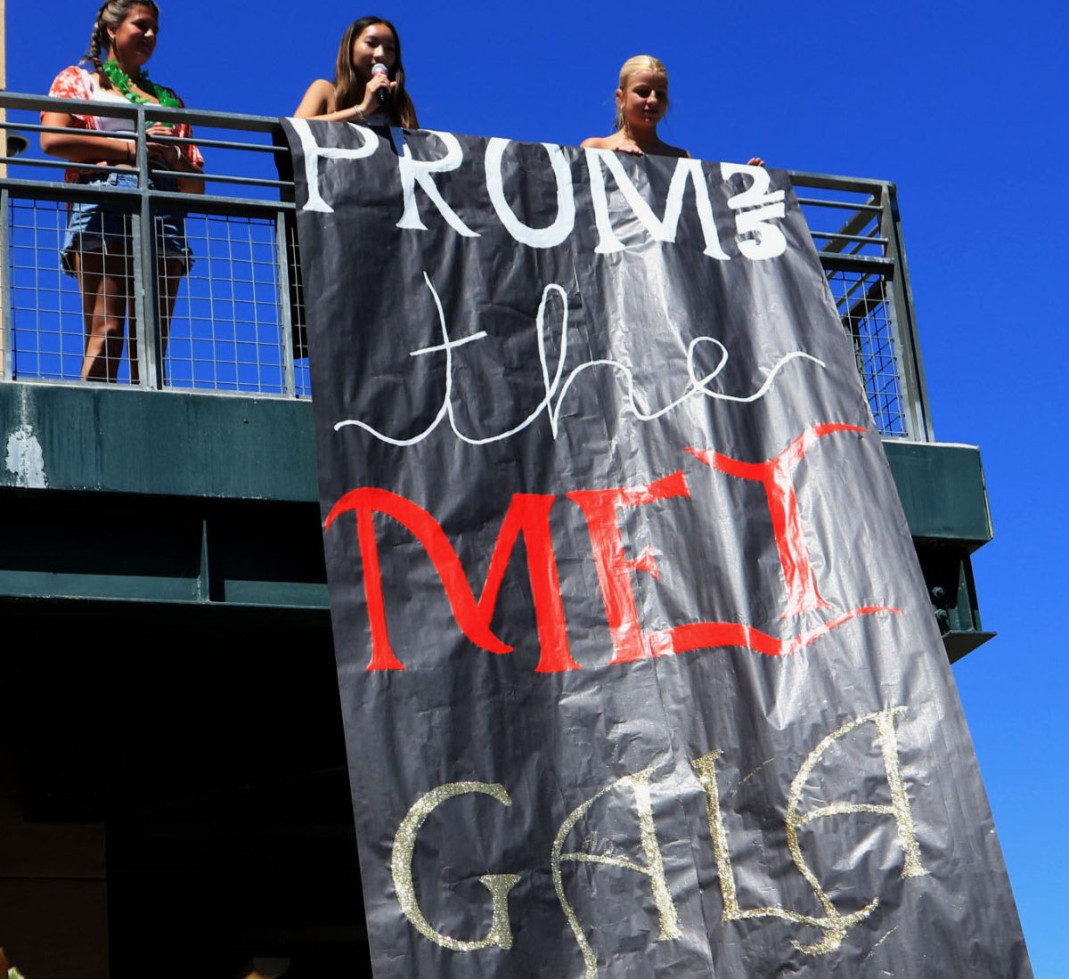Juniors Addy Queen, Kaylaine Le and Cali Murphy announce the prom theme and location by dropping a banner over the stairs.
